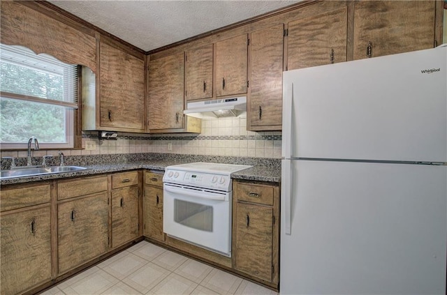 kitchen featuring under cabinet range hood, white appliances, a sink, decorative backsplash, and dark countertops