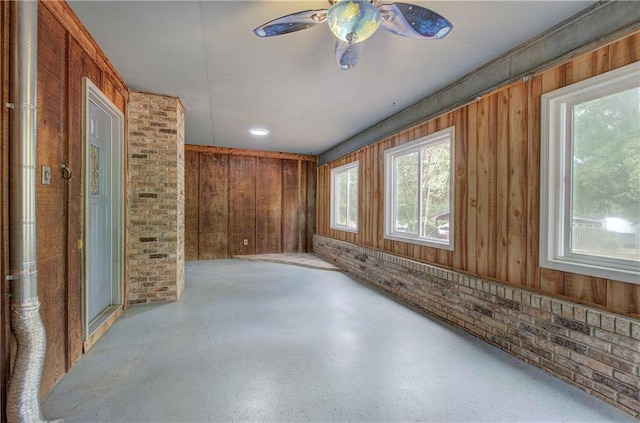 empty room with ceiling fan, brick wall, and wooden walls