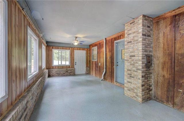 interior space with ceiling fan, brick wall, and wood walls