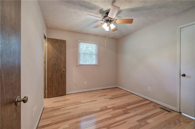 unfurnished bedroom with a textured ceiling, a walk in closet, a closet, light wood-type flooring, and ceiling fan