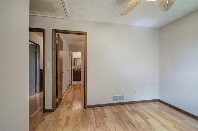 spare room featuring attic access, visible vents, light wood-style floors, and a textured ceiling