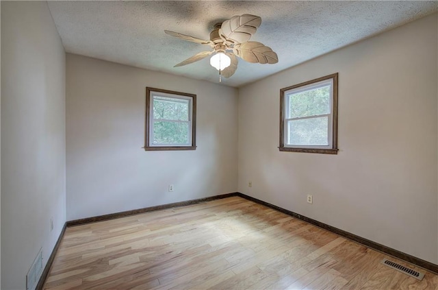 empty room with visible vents, light wood-style flooring, ceiling fan, a textured ceiling, and baseboards