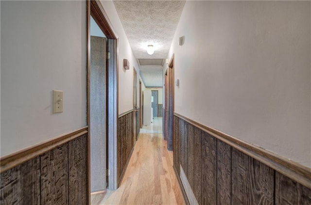 corridor featuring visible vents, wainscoting, wood walls, a textured ceiling, and light wood-type flooring