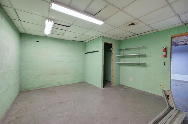 interior space with a paneled ceiling, visible vents, concrete flooring, and concrete block wall