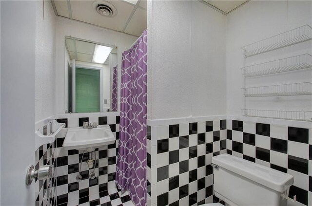 bathroom featuring toilet, tile walls, sink, and curtained shower