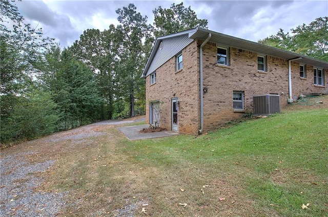 view of side of property with dirt driveway, central AC unit, a lawn, an attached garage, and brick siding