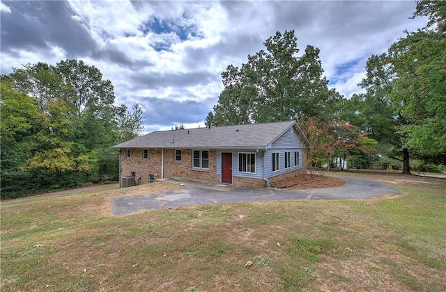 rear view of house featuring driveway, brick siding, central air condition unit, and a yard