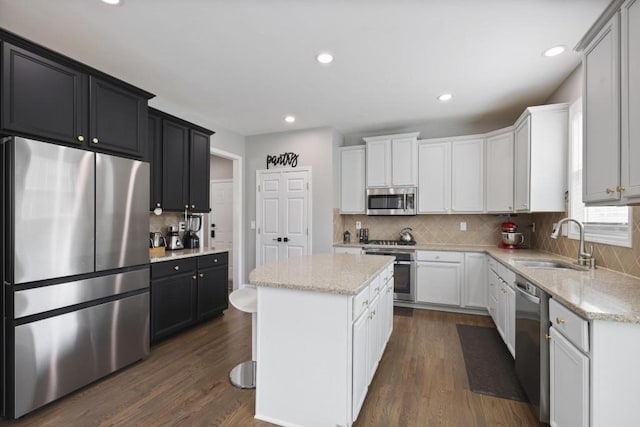 kitchen with dark wood-style flooring, a kitchen island, a sink, appliances with stainless steel finishes, and backsplash