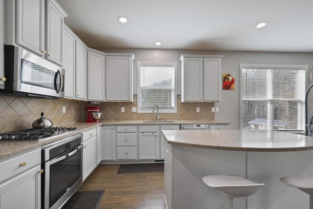 kitchen featuring tasteful backsplash, dark wood-style floors, appliances with stainless steel finishes, a breakfast bar, and a sink