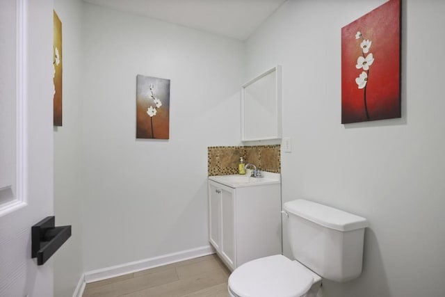 half bath featuring baseboards, toilet, wood finished floors, vanity, and backsplash