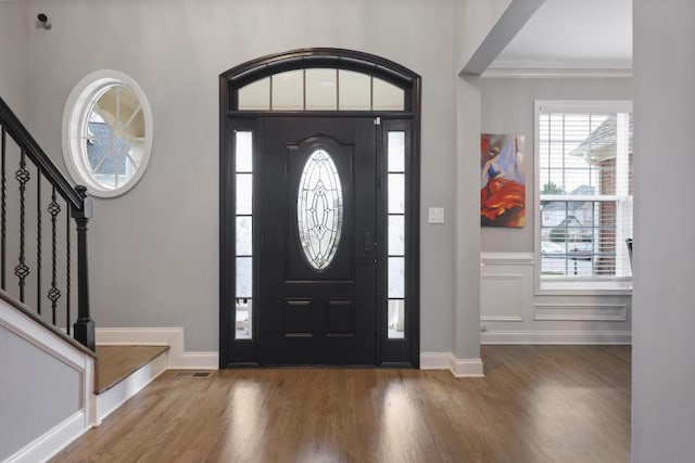 foyer entrance featuring wood finished floors, visible vents, baseboards, stairs, and crown molding