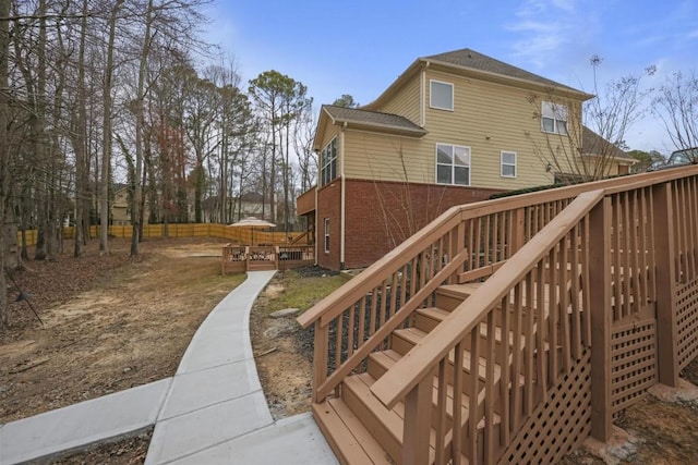exterior space with stairway, brick siding, a wooden deck, and fence