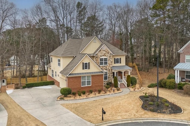 craftsman-style house featuring concrete driveway, metal roof, a standing seam roof, fence, and brick siding