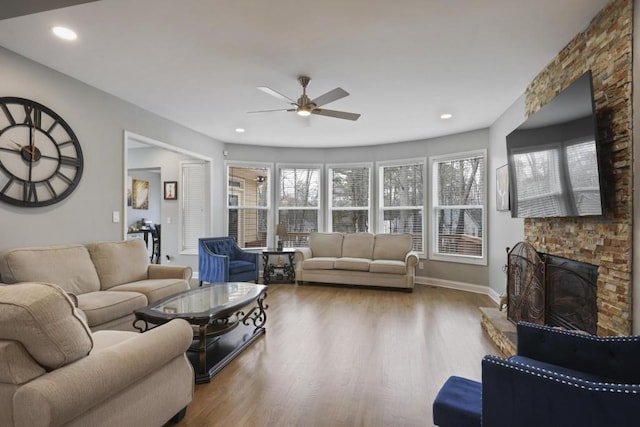 living room with recessed lighting, a ceiling fan, a stone fireplace, wood finished floors, and baseboards