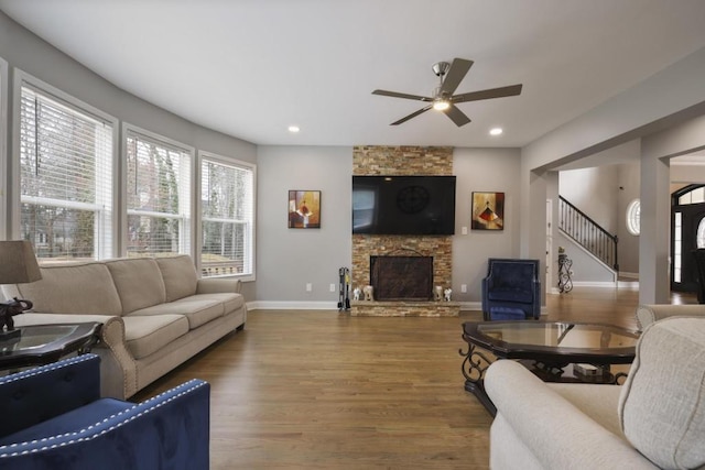 living room with recessed lighting, a stone fireplace, wood finished floors, baseboards, and stairs