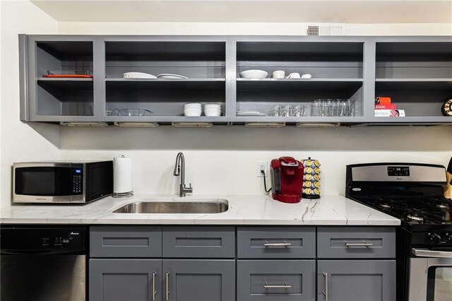 kitchen featuring light stone countertops, stainless steel appliances, gray cabinetry, and sink