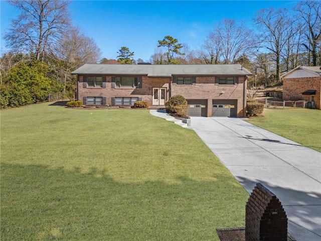 split foyer home featuring brick siding, fence, a front yard, a garage, and driveway