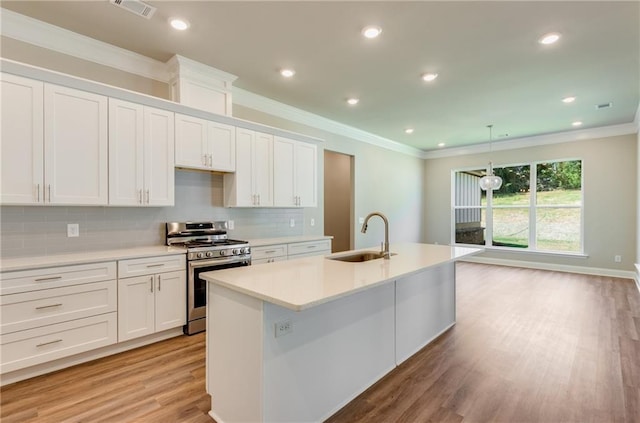 kitchen featuring sink, crown molding, stainless steel gas range, white cabinetry, and a center island with sink