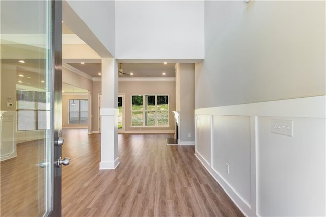 corridor with crown molding, a towering ceiling, and light hardwood / wood-style flooring