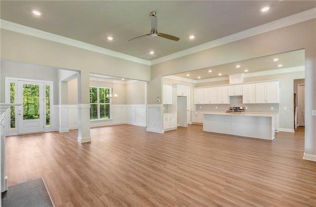 unfurnished living room featuring ornamental molding, ceiling fan with notable chandelier, and light hardwood / wood-style flooring