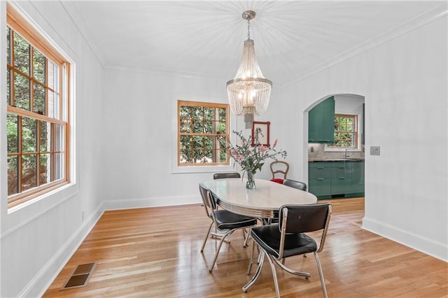 dining area featuring crown molding, a notable chandelier, sink, and light wood-type flooring