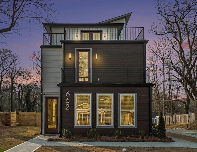 back of house at dusk featuring a balcony and fence