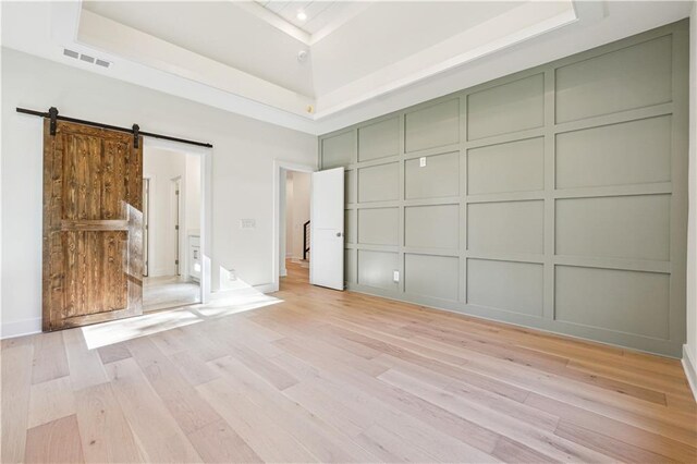 4815 Price Rd, Gainesville, GA 30506 - unfurnished bedroom featuring a decorative wall, light wood-type flooring, a barn door, a towering ceiling, and a raised ceiling