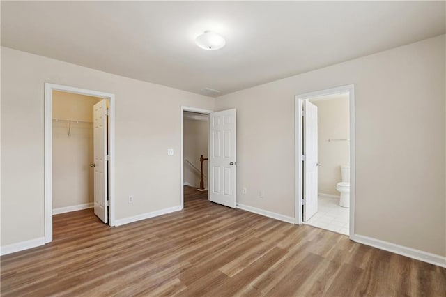 unfurnished bedroom featuring a walk in closet, baseboards, ensuite bathroom, light wood-style floors, and a closet