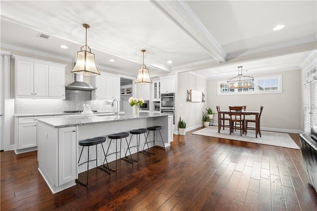 kitchen with dark wood-type flooring, a kitchen island with sink, visible vents, and a sink