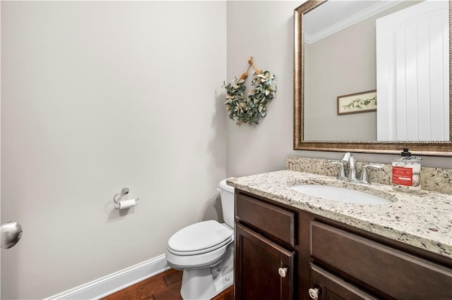 bathroom featuring toilet, wood finished floors, vanity, baseboards, and crown molding