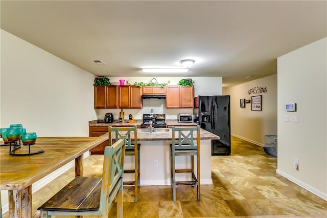 kitchen with brown cabinets, a breakfast bar area, stainless steel appliances, visible vents, and extractor fan