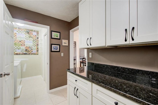 kitchen with white cabinets, dark stone countertops, a textured ceiling, and light tile patterned floors