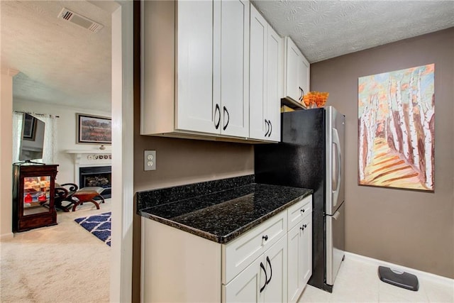 kitchen with white cabinets, dark stone countertops, a textured ceiling, and light colored carpet