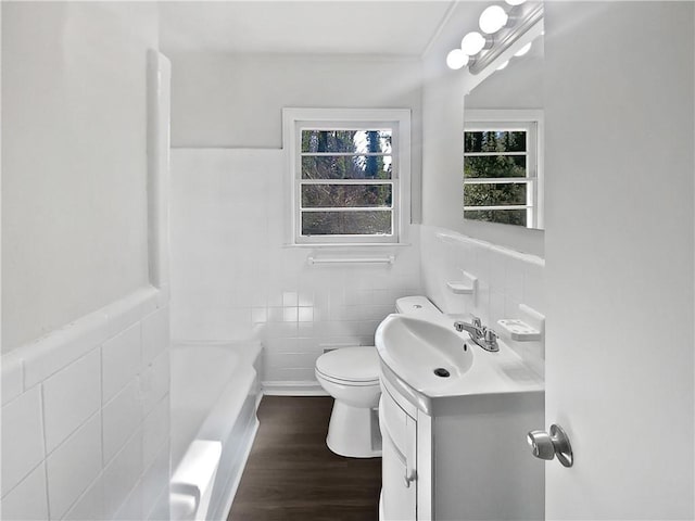 bathroom featuring hardwood / wood-style floors, tile walls, vanity, a washtub, and toilet