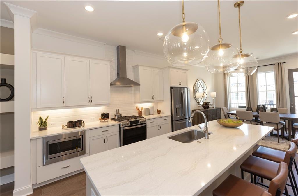 kitchen with appliances with stainless steel finishes, pendant lighting, white cabinetry, sink, and wall chimney range hood