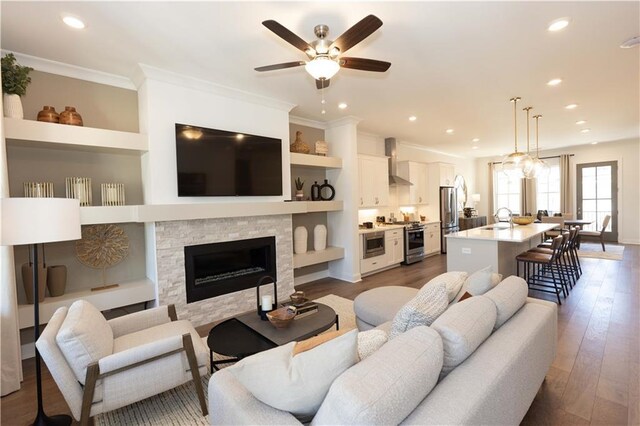 living room featuring built in features, a stone fireplace, sink, dark hardwood / wood-style flooring, and ceiling fan