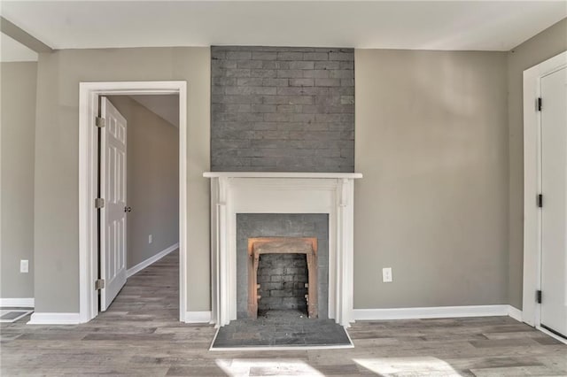 unfurnished living room featuring baseboards, a fireplace with raised hearth, and wood finished floors