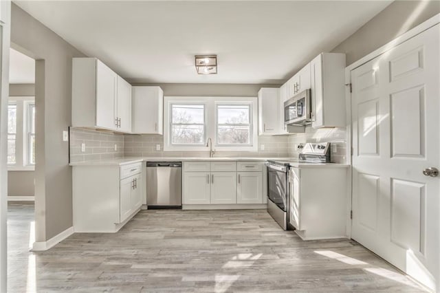 kitchen featuring stainless steel appliances, light countertops, white cabinetry, and backsplash