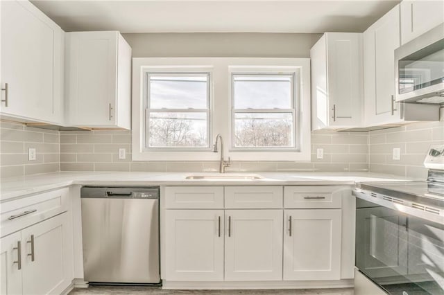 kitchen featuring stainless steel appliances, a sink, white cabinetry, light countertops, and decorative backsplash