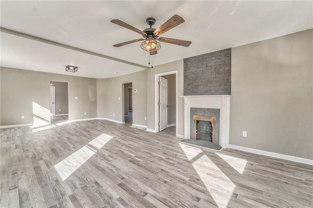 unfurnished living room with a brick fireplace, baseboards, and light wood finished floors