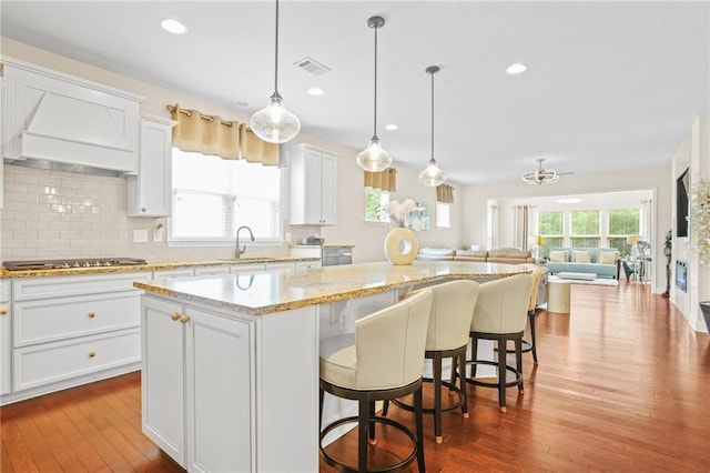 kitchen with visible vents, dark wood-style flooring, a center island, a sink, and backsplash