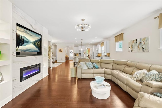 living area featuring an inviting chandelier, built in features, a premium fireplace, and dark wood-type flooring
