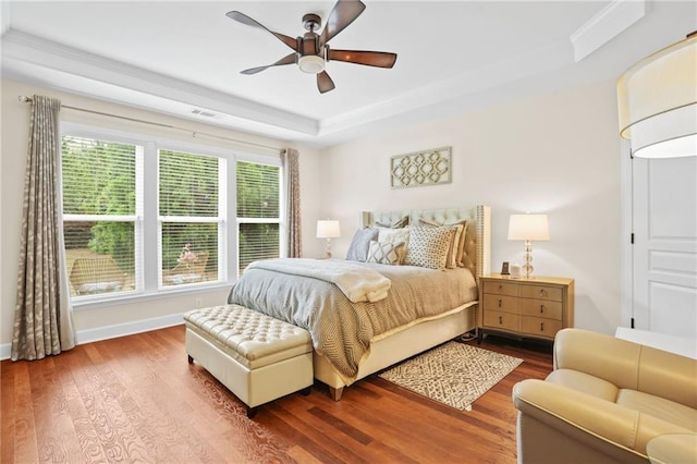 bedroom featuring ceiling fan, a raised ceiling, baseboards, wood finished floors, and visible vents