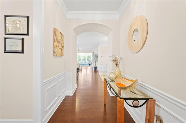 hallway featuring crown molding, wainscoting, a decorative wall, arched walkways, and dark wood-type flooring