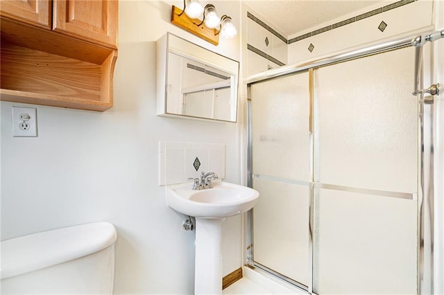 bathroom with a shower stall, toilet, and a sink