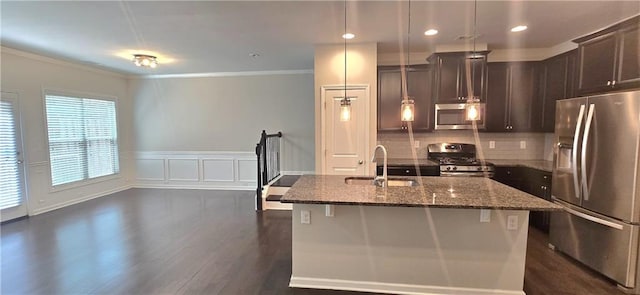 kitchen featuring a sink, dark brown cabinetry, a center island with sink, stainless steel appliances, and dark stone counters