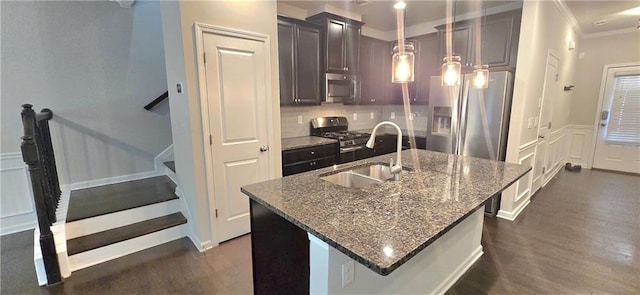 kitchen with a sink, stainless steel appliances, a kitchen island with sink, a decorative wall, and decorative backsplash