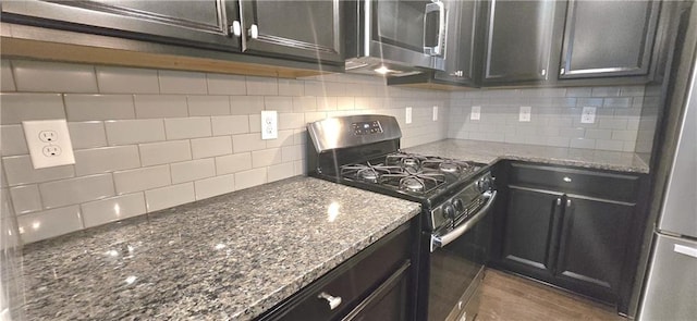 kitchen featuring dark stone counters, appliances with stainless steel finishes, decorative backsplash, and wood finished floors