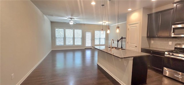 kitchen featuring light stone countertops, appliances with stainless steel finishes, ceiling fan, tasteful backsplash, and an island with sink