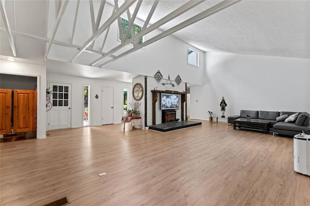 living room with high vaulted ceiling, light wood-type flooring, and a brick fireplace